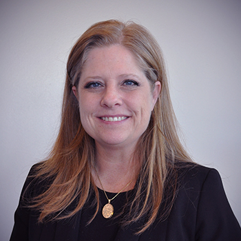 a photo of commissioner Julie Katsel. She is smiling at the camera and wearing a black shirt and gold necklace