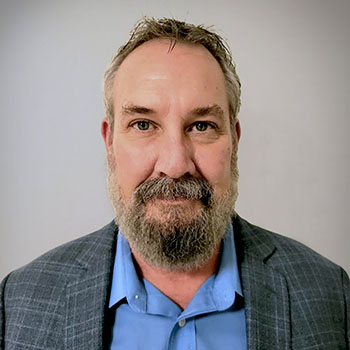 a photo of commissioner Todd Newman. He is looking at the camera and wearing a light blue shirt and checked jacket.